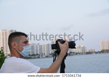 photographer or videographer with a digital camera in a protective mask on his face because of the coronavirus takes a panorama of the city on the water