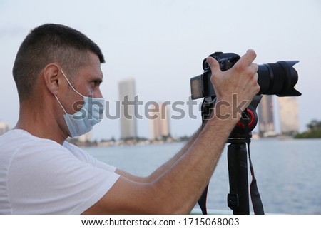 photographer or videographer with digital camera and protective mack on his face at work