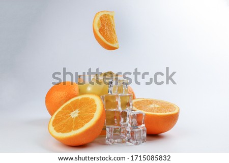 Fresh yellow orange juice in glass with whole floating sliced orange fruit and ice cube on white background