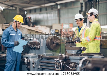 Three technician inspecting complex metal component at machine in factory  Royalty-Free Stock Photo #1715088955