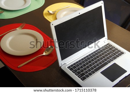 Photo of laptop computer, plates and utensils on a dining table.