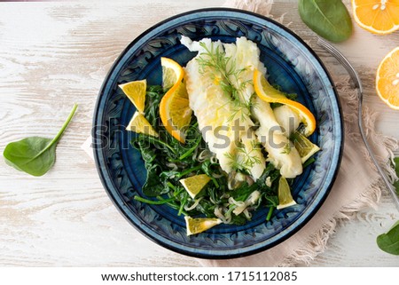 halibut with orange sauce, spinach and shallots on a blue plate on a light wooden table, space for text