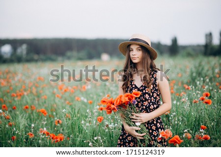 Beautiful young free girl in a hat in a summer field of red poppies with a bouquet. Soft selective focus.