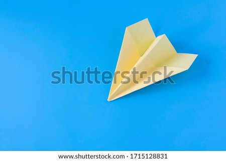 Yellow paper origami plane on a blue background. Close-up.