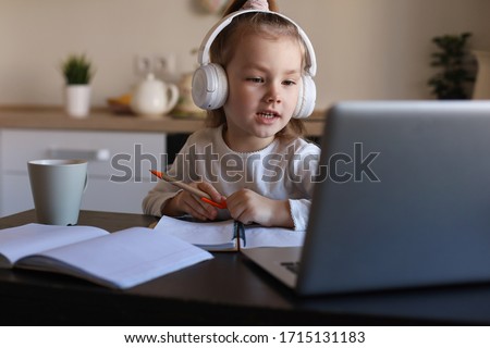 Smiling little girl in headphones handwrite study online using laptop at home, cute happy small child in earphones take Internet web lesson or class on PC.