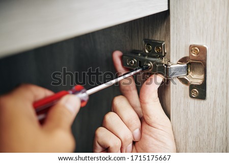 Close-up image of handyman assembling kitchen cabinet and screwing door hinge Royalty-Free Stock Photo #1715175667