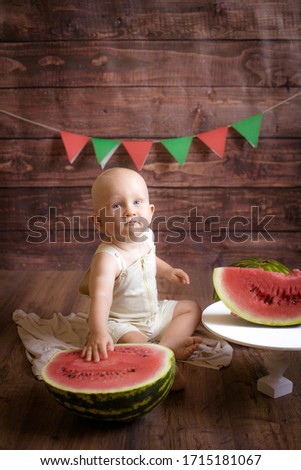 Little cute toddler with blond hair sits and splashes in a basin of water and watermelon on a dark wooden background. Children and fruits. Healthly food
