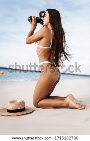 Young woman wear in white bikini with camera shooting on the beach