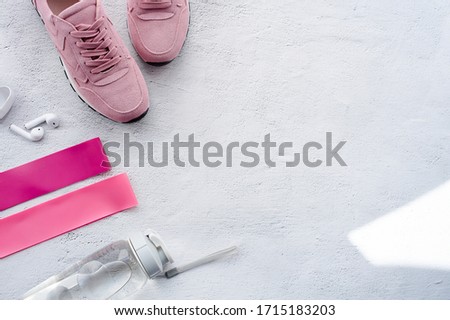 Healthy lifestyle and fitness in sports, morning jogging. Sneakers, wireless headphones, fitness elastic bands and a water bottle on a gray background. Top view and flat lay.