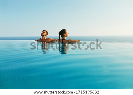 Couple In Love At Luxury Resort On Romantic Summer Vacation. People Relaxing Together In Edge Swimming Pool Water, Enjoying Beautiful Sea View. Happy Lovers On Honeymoon Travel. Relationship, Romance Royalty-Free Stock Photo #1715195632