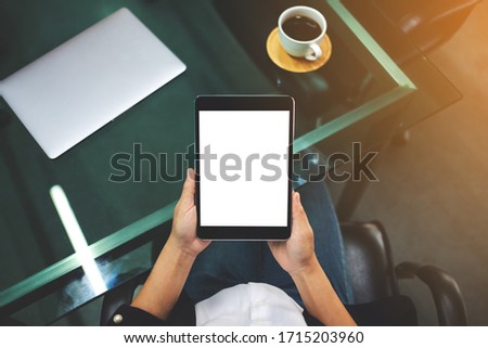 Top view mockup image of businesswoman holding black tablet pc with blank white screen in the office , laptop and coffee cup on the table