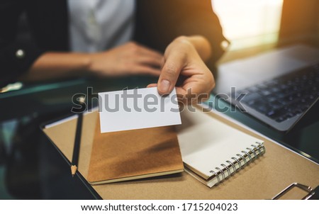 A businesswoman holding and giving a blank business card with laptop computer and paperwork on the table in office