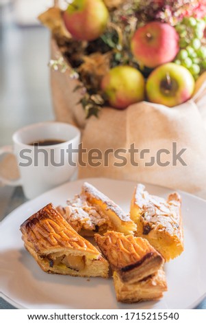The burnt apple pie is on a white ceramic plate. In the background is a white mug of coffee with apples and a bouquet of flowers in soft focus.