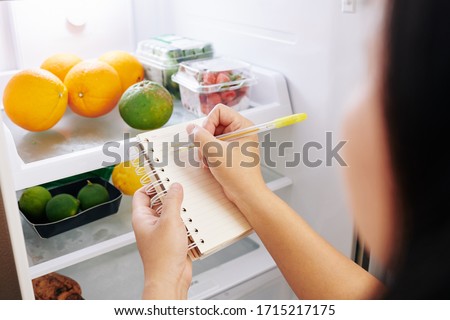 Woman checking refrigerator and making shopping list before going to grocery store Royalty-Free Stock Photo #1715217175