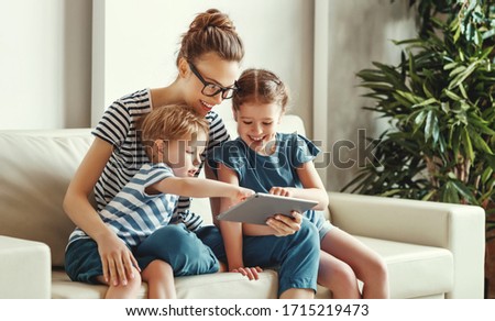 Cheerful young mother with little son and daughter sitting on sofa and playing video game on tablet while spending time together at home
 Royalty-Free Stock Photo #1715219473