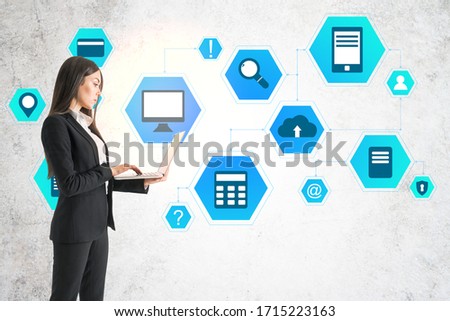 Businesswoman using laptop and drawing cloud computing diagram on concrete wall. Business and technology concept.