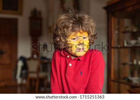 Child with a painted face is watching cartoons. Little boy with a tiger face. Cute child. 