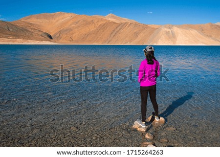 Woman traveller standing on the rocky shores and enjoying a beautiful view at pangong lake.