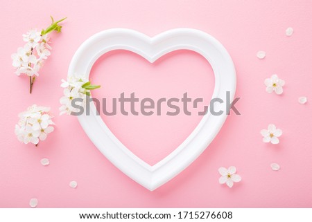 Frame of white heart shape and cherry blossoms on light pink table background. Pastel color. Love and happiness concept. Empty place for cute, emotional, sentimental text, quote or sayings. Closeup.