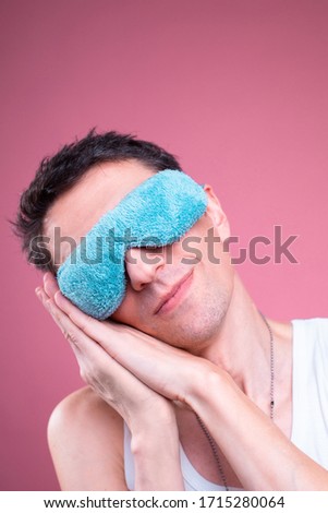 Portrait or vertical picture of nice calm peaceful young man sleep with blue sleeping mask. Hold hands under face. Isolated over pink background