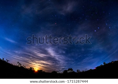 The moon sinking into the black silhouette of the forest and the cloudy starry sky
