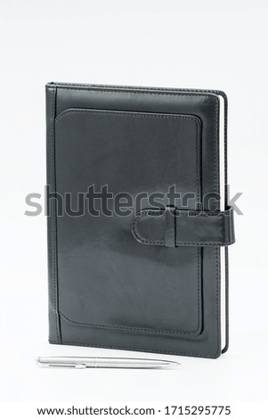 Black leather notebook and a pen on white background. Businessman workspace or diary. Business planning and work day organization
