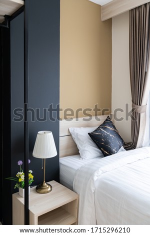 Stylish Bedroom corner with wooden headboard and bed with soft pillows setting with navy blue and yellow painted wall on the background / cozy interior design / modern interior
