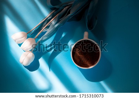 Coffee and spring flowers on blue background. Good mood concept. Blue color filter