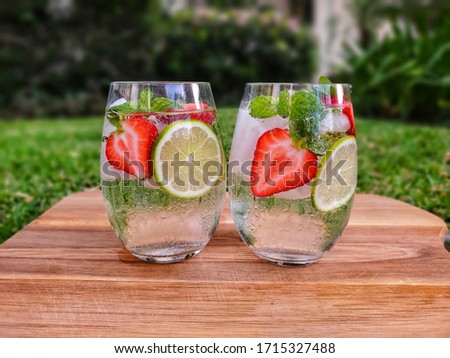 Cocktail strawberry with white rum, lime, sugar, mint, ice and sparking water or club soda on blurred garden background. Summer Concept.