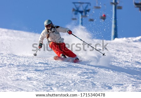 Girl On the Ski. a skier in a bright suit and outfit with long pigtails on her head rides on the track with swirls of fresh snow. Active winter holidays, skiing downhill in sunny day. Woman skier Royalty-Free Stock Photo #1715340478
