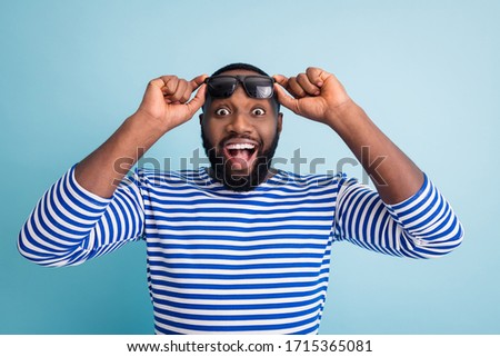 Photo of attractive dark skin guy traveler open mouth see read watch sales season opening advert banner wear sun glasses striped sailor shirt vest isolated blue color background