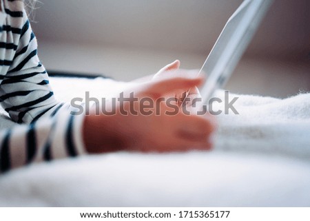 Girl watching cartoon series at home on the bed using wireless tablet computer. Toddler growing with gadget in cozy place. Close-up
