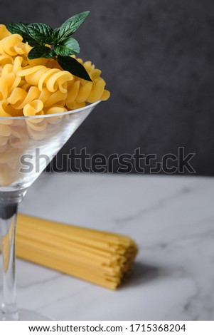 Raw uncooked italian pasta on cocktail glass over white marble. Fusilli. Diet and food concept.