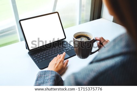 Mockup image of a woman using and touching on tablet touchpad with blank white desktop screen as computer pc while drinking coffee