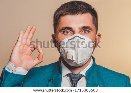 Strong man, businessman in tie and medical mask demonstrates confidence at work in pandemic coronavirus. Shows confidence and calm during the economic crisis with a sign ok on the hand