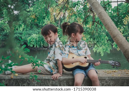 Lovely twin boy and girl stay at home to safe from virus. Lovely twin boy and girl sit leisurely and playing guitar at riverside home. Stay home stay safe concept protect you from virus.