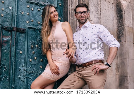 boyfriend and girlfriend are holding hands and looking at the camera on the background of a building with turquoise door.