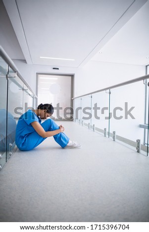 Sad nurse sitting on floor in corridor at hospital