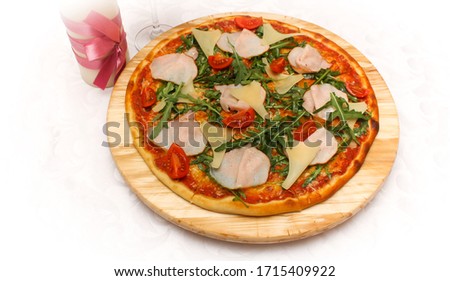 Pizza with tomatoes and arugula leaves on a round tray of wood in bright light