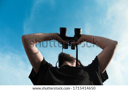 Low angle photo of an ornithologist exploring and observing the birds that fly over him with black binoculars outside