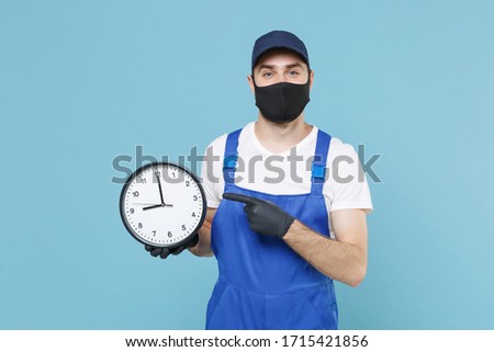 Delivery man in cap tshirt uniform sterile face mask gloves isolated on blue background studio Guy employee courier hold clock Service quarantine pandemic coronavirus virus covid-19 2019-ncov concept