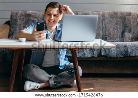 Focused student man studying remote on laptop sit on floor in living room, happy male student freelancer using looking at computer and doing home work
