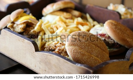 Wooden tray full of chips and burgers. Close-up view of platter with opened hamburger and fries.