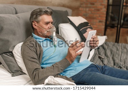Man doing inhalation through oxygen mask at home bedroom and use laptop. Royalty-Free Stock Photo #1715429044