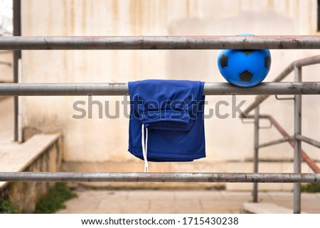 Blue soccer ball and blue soccer shorts hanging over metal rails of a city alleyway