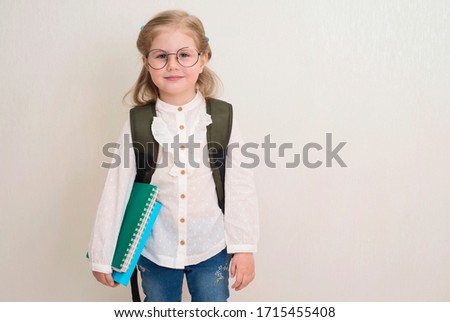 Portrait of smiling confident school girl or preschooler with books and backpack  standing on white background. Education and back to school concept.
