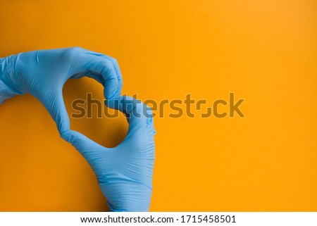 Two hands in blue medical gloves folded in the shape of a heart on an orange background Royalty-Free Stock Photo #1715458501