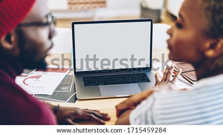 From above side view of crop black man and woman sitting at table with netbook and documents while discussing business strategy and looking at each other