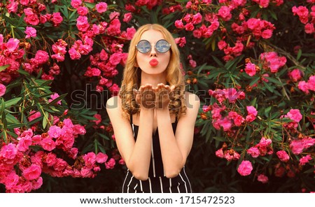 Fashion portrait beautiful young woman blowing red lips sending sweet air kiss over pink flowers background