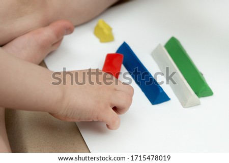 red bar of plasticine in the hand of a child. multi-colored pieces on the background